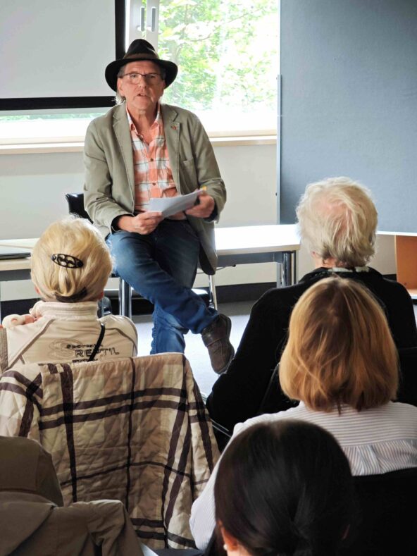 Jo Köhler sitzt auf einem Tisch und spricht zum Publikum