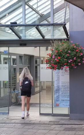 Ein Lesezeichen an der Glastür der Andreaspassage. Eine junge Frau betritt die Einkaufspassage.