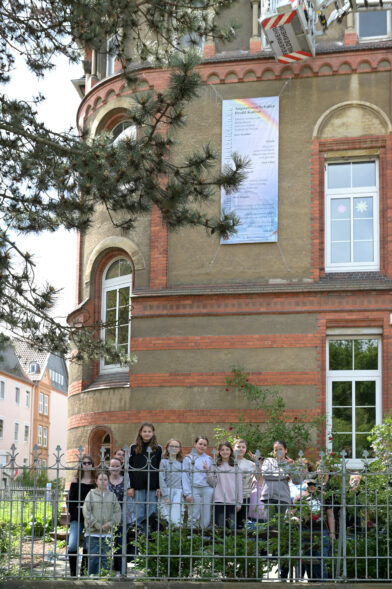 Das Lesezeichen hängt an der Schule. Die Schüler:innen stehen vor der Schule.