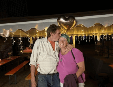 Grit und Klaus Belkot vor einer Partyzeltgarnitur, geschmückt mit vielen Lichterketten. Ein goldener Herzballon schwebt im Hintergrund.